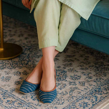 Person wearing blue patterned flats on a patterned rug with a teal couch in the background